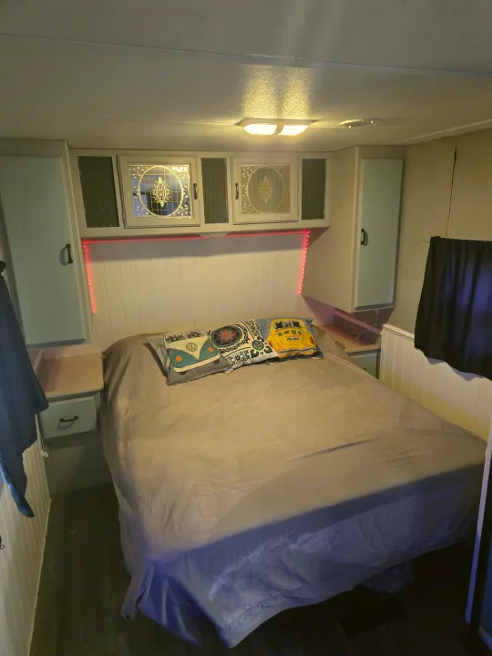 Cozy RV rental bedroom featuring a comfortable bed, custom overhead cabinets, and red accent lighting.. Fleetwood Mallard 2004