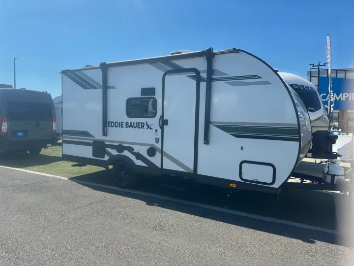 A sleek white Eddie Bauer travel trailer with green and gray stripes, ideal for RV rental. Seen outdoors on asphalt with blue sky.. Heartland Eddie Bauer 2025