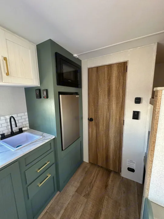Explore this RV rental's compact kitchen: green cabinets, white subway tile backsplash, sink, microwave, fridge, and wood-look floor.. Heartland Eddie Bauer 2025