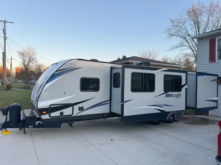 Light gray travel trailer with slide-outs extended, parked on a concrete driveway, ready for your RV rental adventure.. Keystone RV Bullet Ultra Lite 2019
