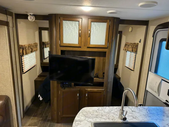 Inside an RV rental: a compact, functional interior with a TV, kitchen counter, and private sleeping nooks.. Keystone RV Bullet Ultra Lite 2019