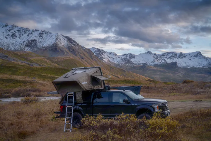 Adventure awaits! Black F-150 with a rooftop tent, a rugged RV rental option, parked in snowy mountains.. Ford Ford F150 2020