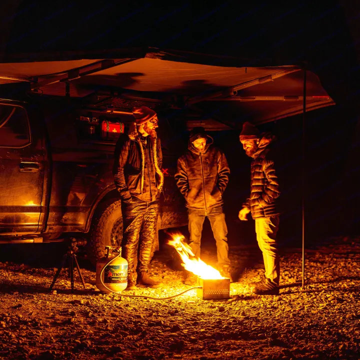 Night camping under an RV rental awning. Three men gathered around a cozy fire pit, enjoying the outdoors.. Ford Ford F150 2020