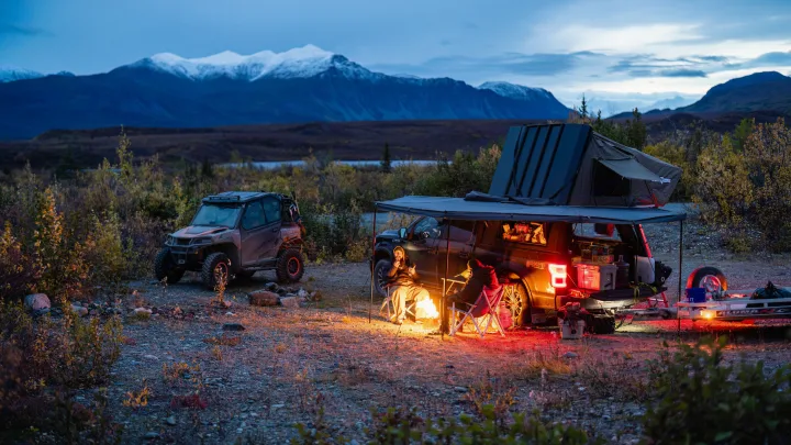 People enjoy a campfire at dusk. An overland truck & UTV offer an RV rental alternative for mountain adventures.. Ford Ford F150 2020