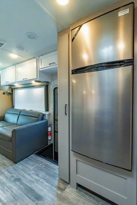 Modern RV rental interior features a large stainless steel refrigerator, comfortable gray sofa, and storage cabinets.. Thor Motor coach Geneva 2025