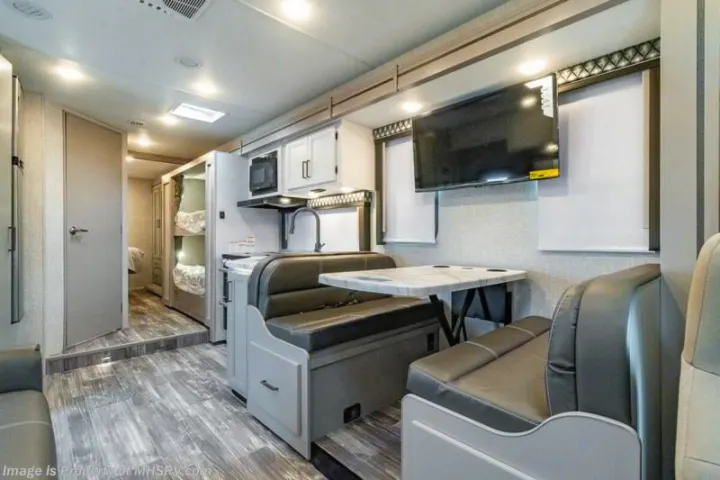 This RV rental interior features a kitchen, comfortable dinette, bunk beds, and a wall-mounted TV.. Thor Motor coach Geneva 2025