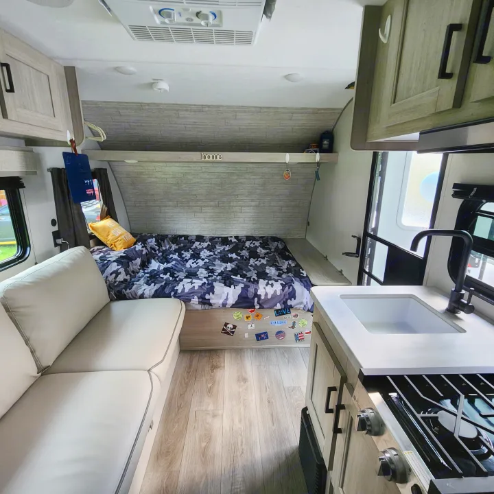 Cozy RV rental interior: camo bed, light sofa, and compact kitchen, ready for adventure.. Coachmen Catalina 2024