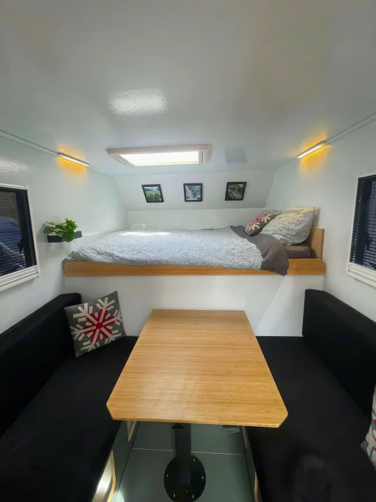 RV rental interior showing an elevated bed above a dining area with a wooden table and benches. Cozy and functional space.. Ford Lightning 2024