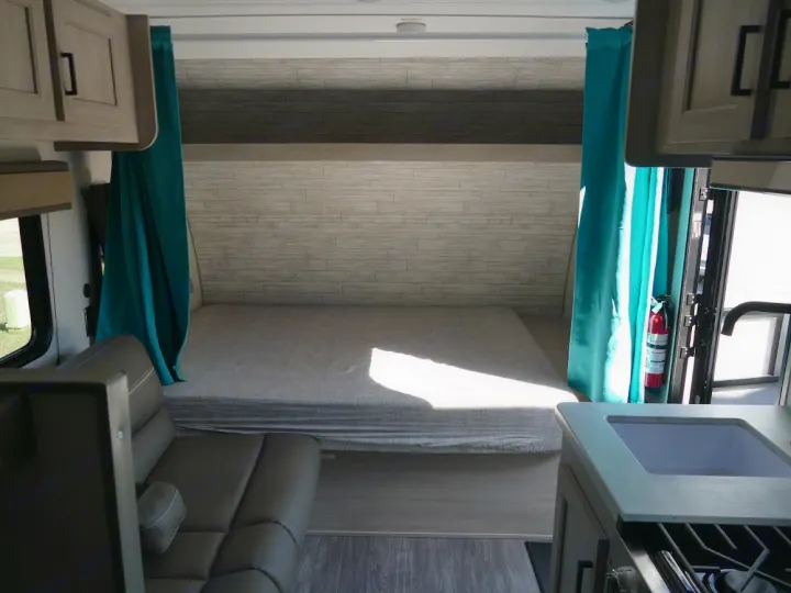 Cozy RV rental interior featuring a comfortable bed, compact kitchen with sink and stovetop, and a sofa seating area.. Forest River Aurora 2024