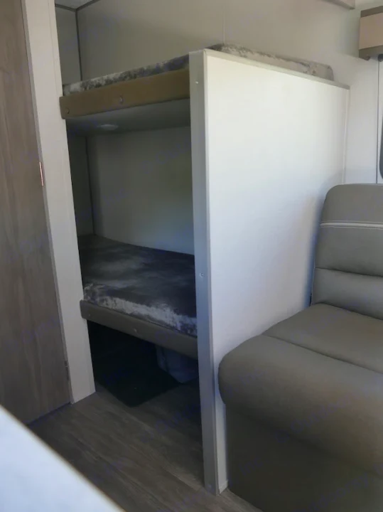Cozy bunk beds with dark mattresses inside an RV rental, featuring a light and a grey sofa nearby. Ideal for family trips.. Forest River Aurora 2024