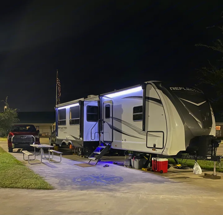A well-lit rv rental, a Grand Design Reflection RV, parked at night. A red truck, picnic table, and resort emblem complete the scene.. Grand Design Reflection 2024
