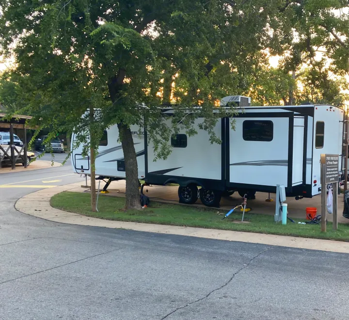 A spacious white rv rental with extended slide-out at a green, tree-shaded campsite.. Grand Design Reflection 2024