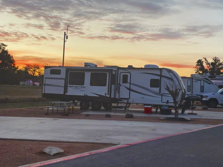 Serene sunset view of a Grand Design Reflection RV rental parked at a campsite with a picnic table.. Grand Design Reflection 2024