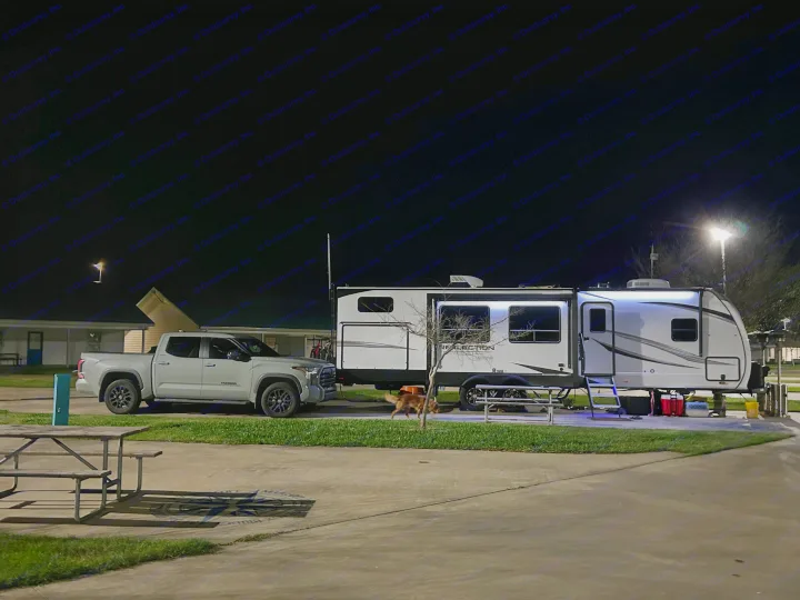 Experience RV camping: a white truck and Reflection RV rental parked under night lights at a campsite.. Grand Design Reflection 2024