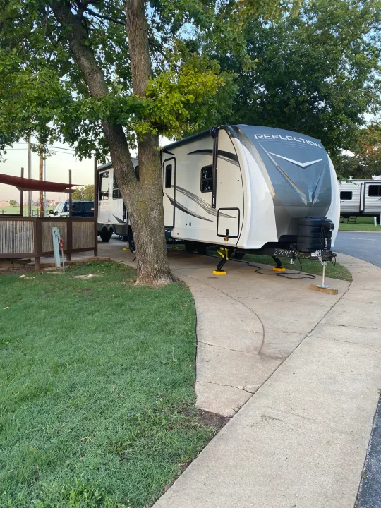 A 'Reflection' RV rental travel trailer is set up on a concrete pad at a peaceful, tree-shaded campsite.. Grand Design Reflection 2024