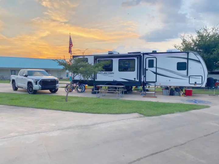 Sunset view of a white truck & Grand Design Reflection RV at a campsite. Ideal for your rv rental experience!. Grand Design Reflection 2024