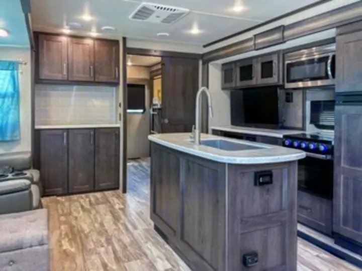 Modern RV rental interior features a spacious kitchen with island, dark wood cabinets, and living area for comfortable travel.. Grand Design Reflection 2024