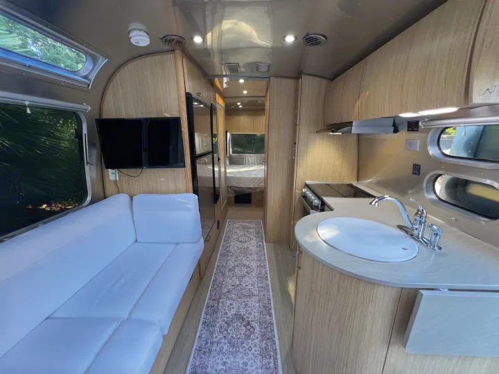 Modern travel trailer RV rental interior: kitchen, comfy sofa with TV, and a rear bedroom. Ready for adventures!. Airstream Flying Cloud