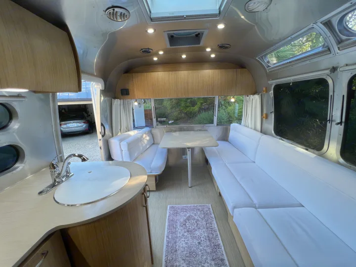 Experience comfort in this Airstream RV rental: modern interior features white lounge seating, a dining area, and a sleek kitchenette.. Airstream Flying Cloud