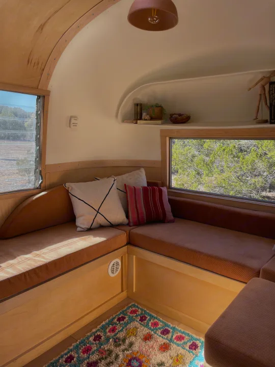 This cozy RV rental features a comfortable corner seating area with corduroy cushions, natural wood, and bright views.. Airstream Safari 1964
