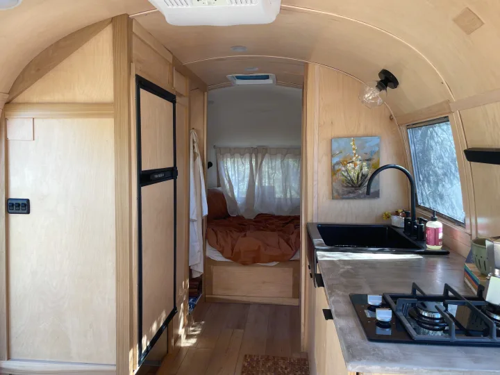 Step inside this modern RV rental! Light wood interior features a full kitchen with black sink, gas hob, and a cozy bedroom.. Airstream Safari 1964