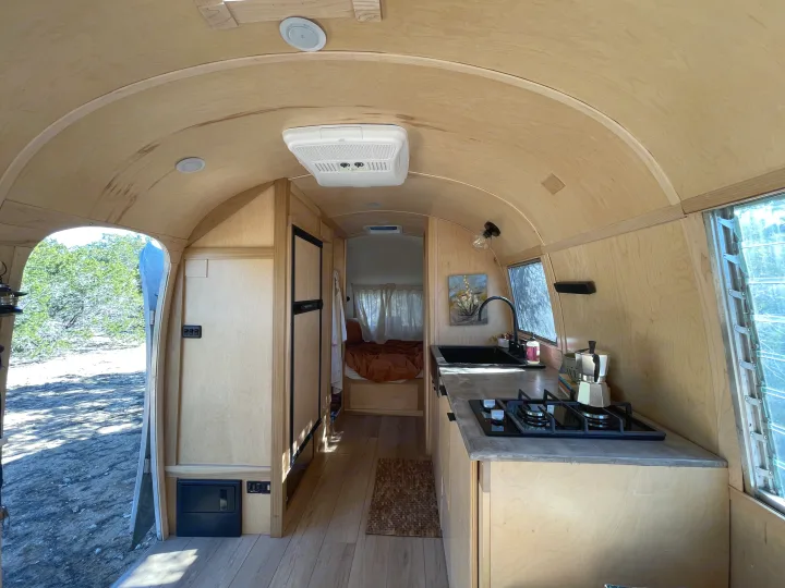 This rv rental interior features a cozy, wood-paneled design with a kitchen on the right and a bedroom at the back.. Airstream Safari 1964