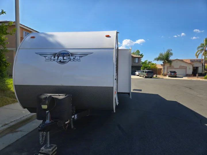 White Shasta RV with slide-out extended, parked on a sunny street. Consider this ideal for an RV rental!. Forest River Shasta 2021