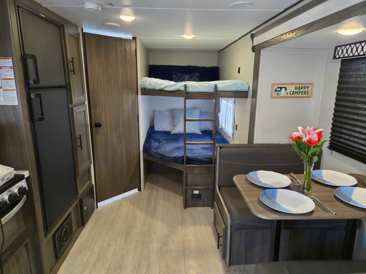 Cozy RV rental interior featuring bunk beds, a fully set dinette, and a compact kitchen area with a refrigerator.. Forest River Shasta 2021