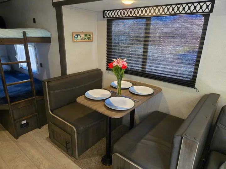 An RV rental's inviting interior: A dining area with place settings and flowers, plus cozy bunk beds on the left.. Forest River Shasta 2021