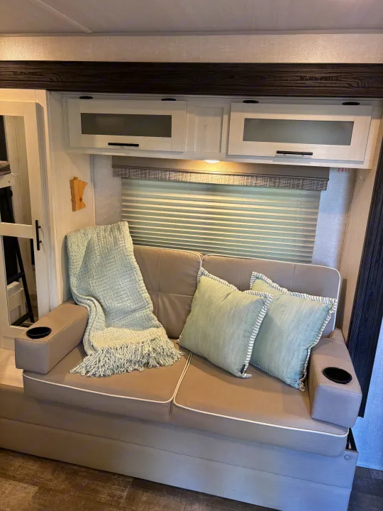 Comfortable RV rental interior: cozy sofa, light blue pillows & blanket, window, and overhead cabinets.. Forest River R-Pod 2022