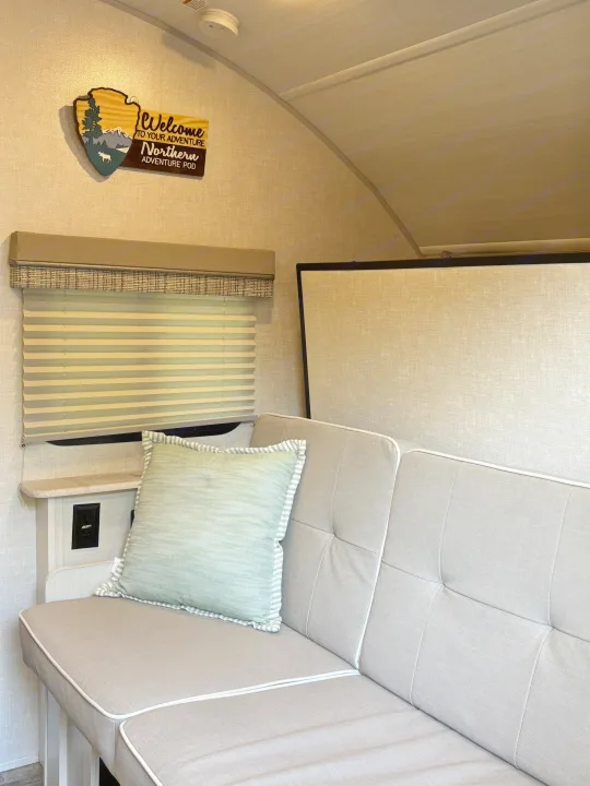 Welcoming RV rental interior: comfortable light grey sofa with green pillow, adventure sign, and window blinds.. Forest River R-Pod 2022