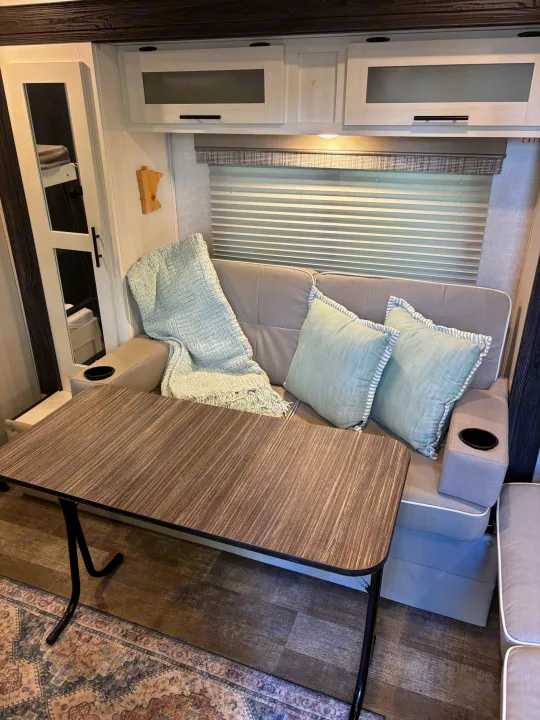 Inside an RV rental: a compact dinette with cozy grey seating, pale blue pillows, and a wooden table. Bunk beds visible.. Forest River R-Pod 2022
