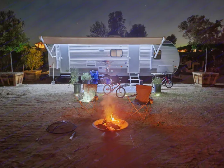 Nighttime RV rental setup: a brightly lit travel trailer, warm campfire, chairs, and bikes ready for adventure.. Forest River Shasta 2021