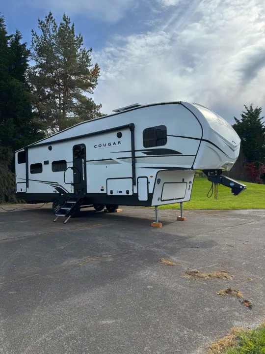 Modern white Cougar fifth-wheel RV rental parked on pavement, with stabilizing jacks set and an awning retracted.. Keystone Cougar 2025