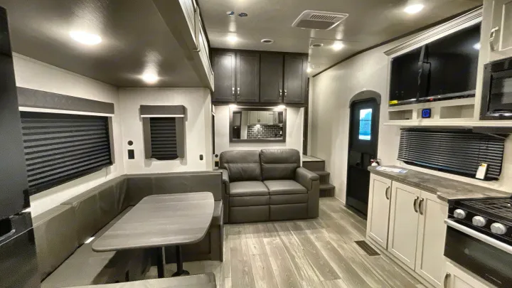 Spacious RV rental living area: gray dinette, sofa, and a modern kitchen with TV. Light wood floors enhance comfort.. Keystone Cougar 2025