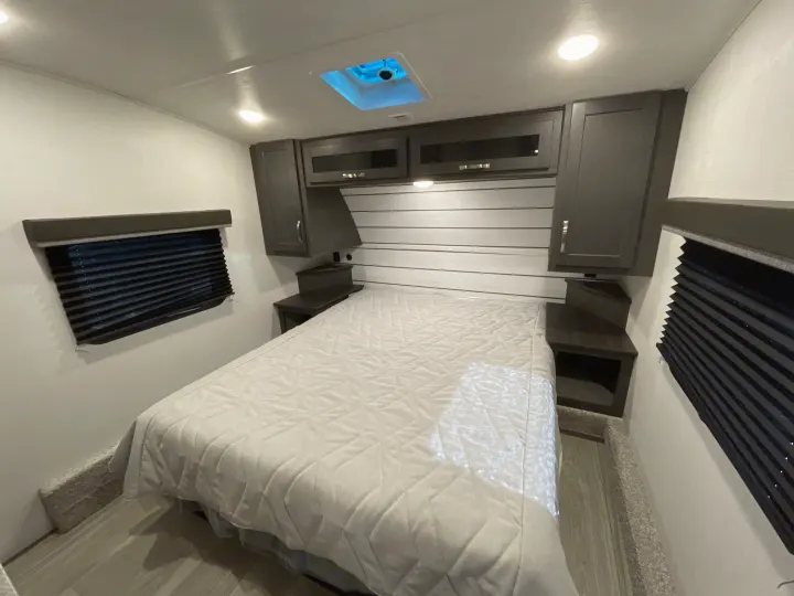 Cozy RV rental bedroom with a bed, dark cabinets, window blinds, and a blue-lit skylight. Ideal for travel adventures.. Keystone Cougar 2025