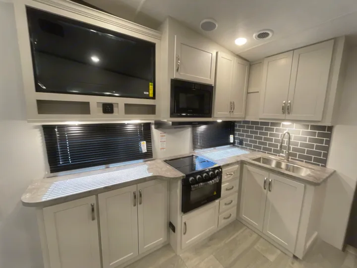 Modern RV rental kitchen with sleek grey and white design, including a stovetop, sink, microwave, and TV.. Keystone Cougar 2025