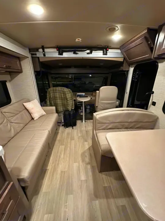 RV rental interior view showcasing a comfortable sofa, dinette, and front driving cabin with an overhead bunk.. Winnebago Adventurer 2021
