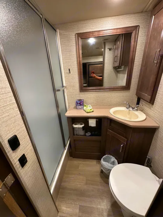 Compact RV rental bathroom featuring a shower with frosted door, vanity with sink, mirror, and toilet.. Winnebago Adventurer 2021