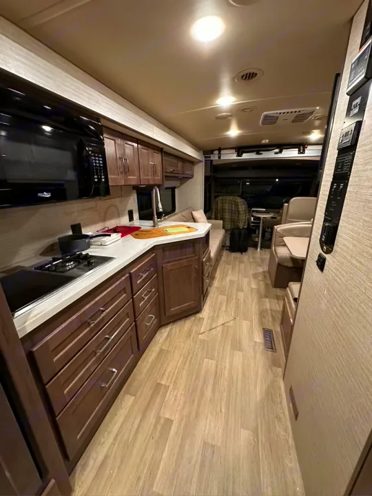 Modern rv rental interior showing full kitchen with dark cabinets, light wood-look floor, and bright, spacious living area.. Winnebago Adventurer 2021