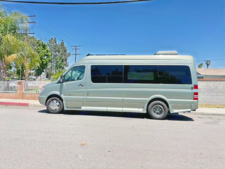A sleek light green Mercedes-Benz Sprinter RV rental with tinted windows and a rooftop AC, parked curbside on a clear day.. Roadtrek Roadtrek Class B 2013