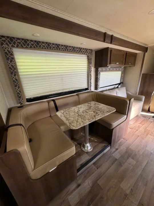This RV rental interior features a cozy U-shaped dinette with tan cushions and granite-style table, ideal for dining and lounging.. Jayco Redhawk 2019