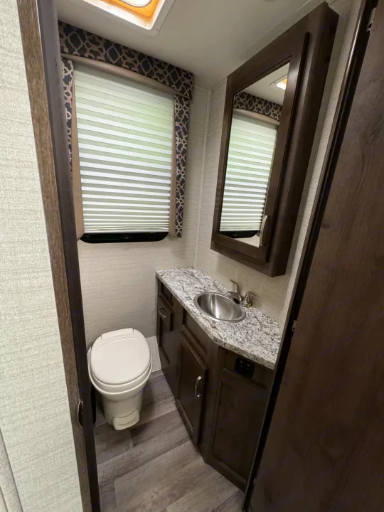 Inside an RV rental: a compact bathroom with a toilet, sink, mirror, and window. Perfect for your next road trip!. Jayco Redhawk 2019
