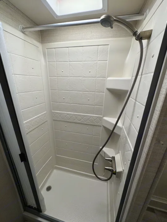 Clean shower unit in an RV rental, with a handheld showerhead, corner shelves, and a clear door for convenience.. Jayco Redhawk 2019