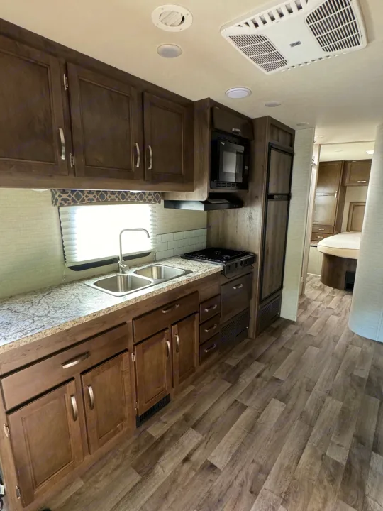 Stylish RV rental interior with a well-equipped kitchen: wood cabinets, granite-look counters, sink, appliances, and bedroom view.. Jayco Redhawk 2019