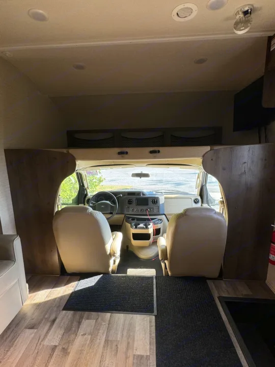 RV rental interior looking towards the cockpit with beige seats, dashboard, and overhead bunk. Spacious camper cabin.. Jayco Redhawk 2019