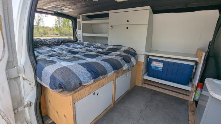 RV rental camper van interior features a comfy bed with storage below, custom shelving, and a cooler on a slide-out tray.. Gmc Savana 2011