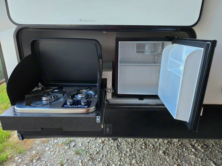 View of an RV rental's outdoor slide-out kitchen, featuring a FlameKing two-burner stove and an open mini-fridge.. Dutchman Astroia 2022