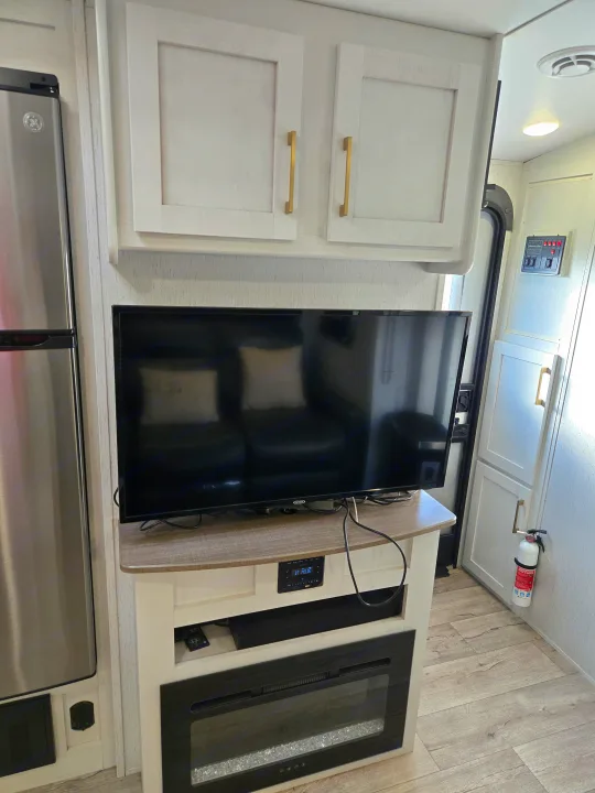 RV rental interior: living area with TV, soundbar, electric fireplace, and overhead storage. Refrigerator on the left.. Dutchman Astroia 2022