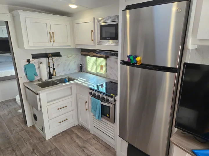 RV rental with a bright kitchen: white cabinets, stainless steel fridge, microwave, stove, double sink, and wood floor.. Dutchman Astroia 2022